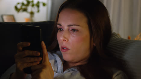 Close-Up-Of-Woman-Lying-On-Sofa-At-Home-At-Night-Streaming-Or-Looking-At-Online-Content-On-Mobile-Phone